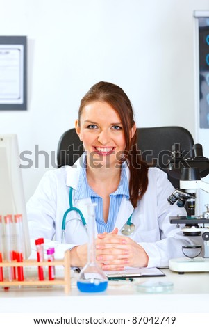 Smiling female medical doctor sitting at table in cabinet