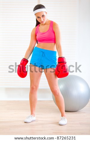 Serious fit woman in boxing gloves standing in angry pose at living room