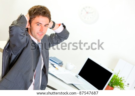 Pleased modern businessman relaxing on armchair at office desk
