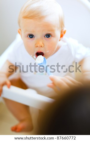 Eat smeared adorable baby girl in baby chair feeding by mother
