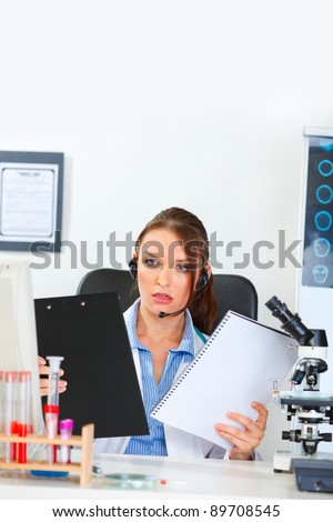 Confused doctor woman with headset looking on clipboard and notepad in hands
