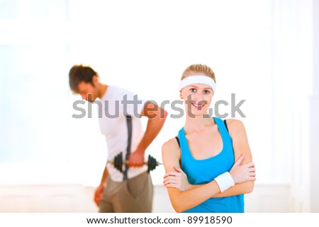 Portrait of slim girl in sportswear and man making sport exercises in background