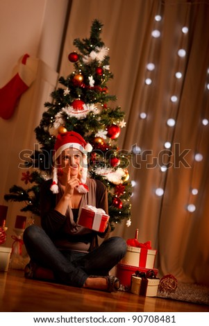Interested girl near Christmas tree with present box trying to guess what\'s inside