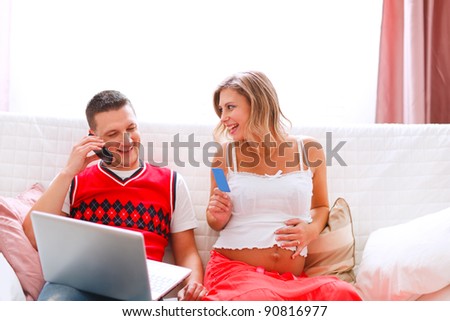 Young man with happy pregnant wife confirming online purchase by phone