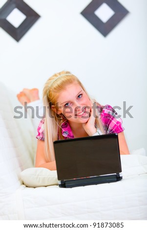 Smiling young woman laying on white couch with laptop
