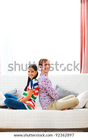 Cheerful young couple sitting on sofa back to back