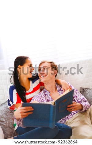 Laughing young couple sitting on couch and looking in photo album