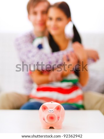 Piggy bank on table and happy young couple in background