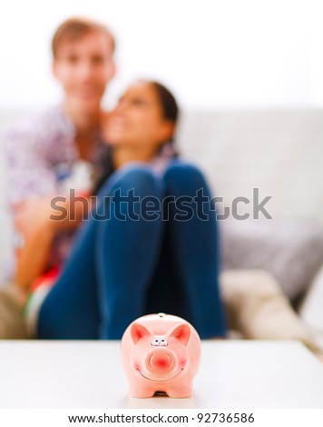 Piggy bank on table and happy young couple in background