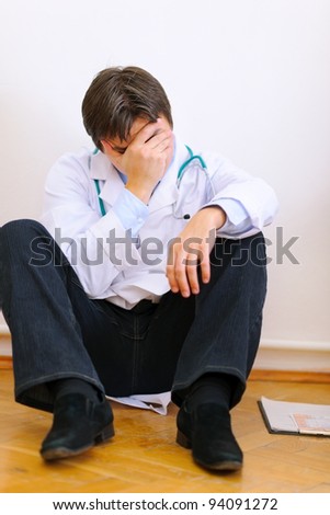 Upset medical doctor sitting on floor