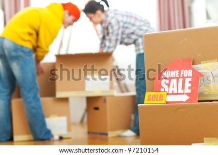 Home for sale sign with sold sticker and unpacking young family in background
