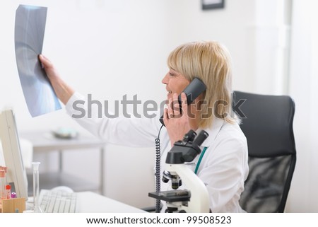 Middle age doctor woman speaking phone and looking on patients roentgen