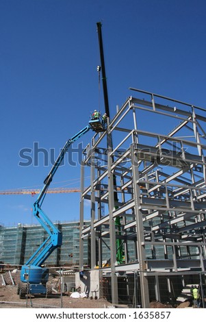 Cherry picker and crane beside metal frame of new building
