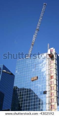 crane lifting load to top of blue glass skyscraper
