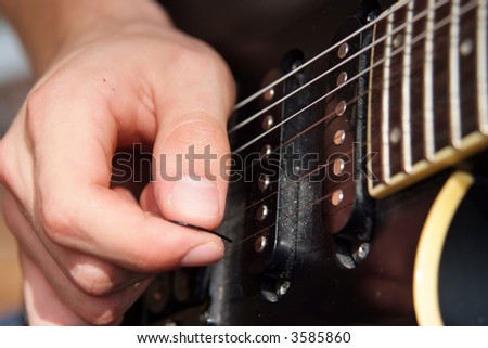 Close up of a hand playing with a pick on an electric guitar