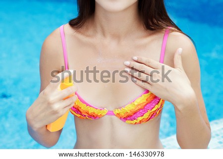 girl putting solar cream on body on summer day outdoors near pool under sunshine