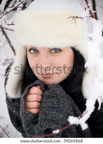 funny girl in fur cap and sweater sitting under snow bush