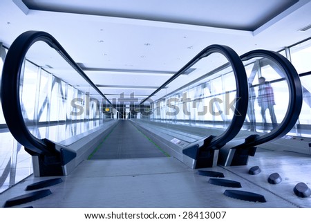 People move in grey corridor with escalators in office centre