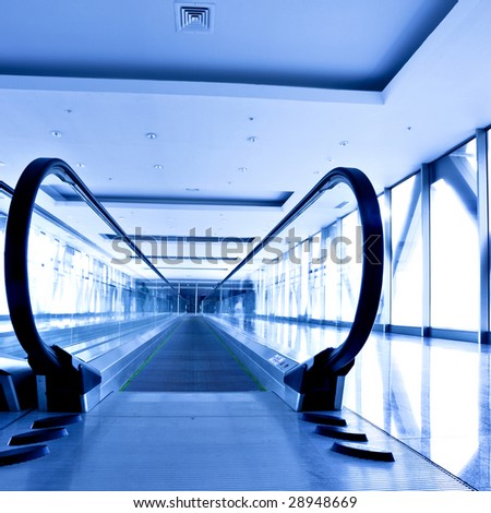 People move in grey corridor with escalators in office centre