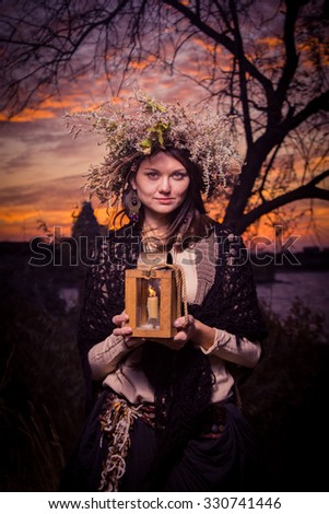 Dark beautiful woman in a mysterious stone village with lamp in her hand in sunset. Fantasy and halloween concept