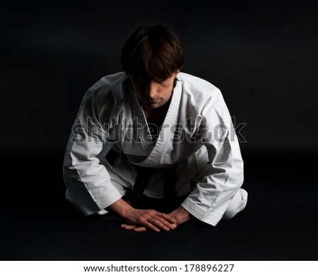 Karate man in kimono making traditional bow on a black background