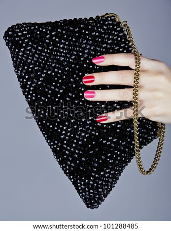 hand of a young woman with bright fashion manicure with pink and red nails holding a vintage beaded bag.