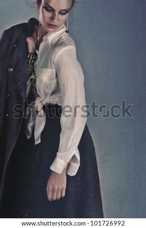 sad young woman in lace skirt and tied shirt wearing vintage coat over grunge background with space for text.