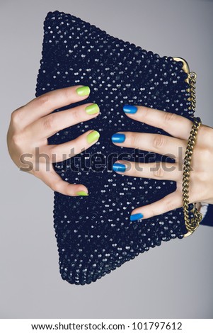 hand of a young woman with bright fashion manicure with green and blue nails holding a vintage beaded bag