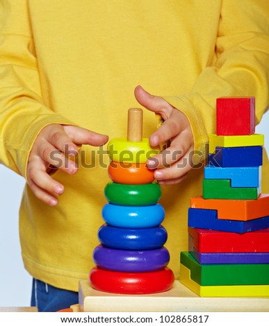 little 3 year old toddler boy playing with bright wooden pyramid over light studio background