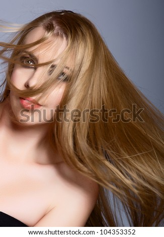 beautiful woman with long blond hair blowing over her face against the blue studio background.