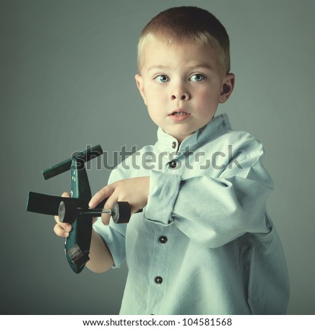 young 3 year old boy wearing blue shirt playing with wooden toy airplane in his hand on blue studio background.