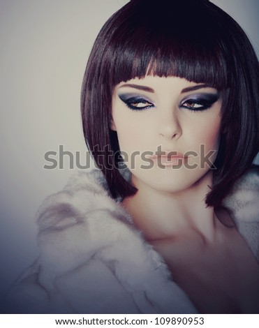 beautiful young woman with short brown hair in white fur coat wearing smoky purple eyeshadow and dramatic eyeliner.