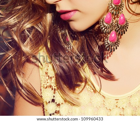 closeup of blond woman with long wet curly hair wearing pink lipstick and gold and pink neon earrings