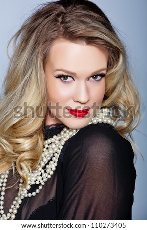 portrait of a beautiful young woman with curly blond hair and glamour make-up with red lips wearing a black blouse and pearls