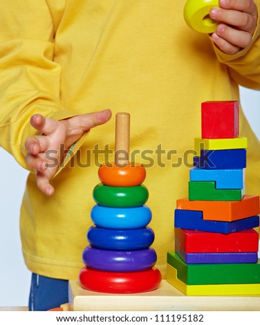 little 3 year old toddler boy playing with bright wooden pyramid over light studio background