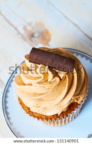 Coffee and chocolate cream cupcake with a swirl on a white plate against grunge wooden background