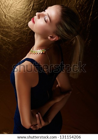 beautiful woman with ponytail wearing stretch dress on gold background with artistic lighting