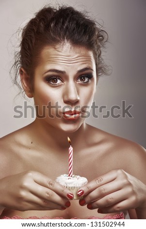 Artistic portrait of a teenage girl making a wish as she holds a birthday cupcake with a candle on studio background