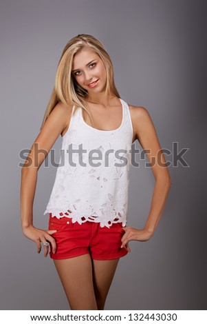 beautiful young woman wearing red shorts and white lace fashion top smiling on gray studio background