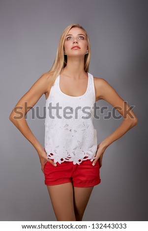 beautiful young woman wearing red shorts and white lace fashion top smiling on gray studio background