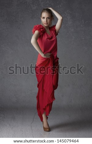 Beautiful blond woman in red pleated skirt and ruffled top balancing on one foot on grunge studio background - full length