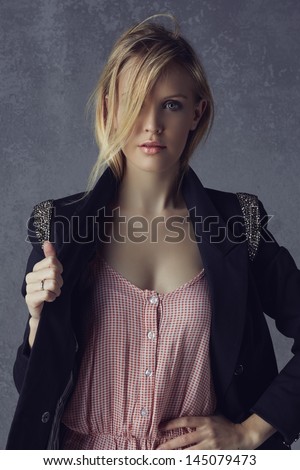 beautiful young blond woman with messy hair in a black blazer and pink top on grunge studio background