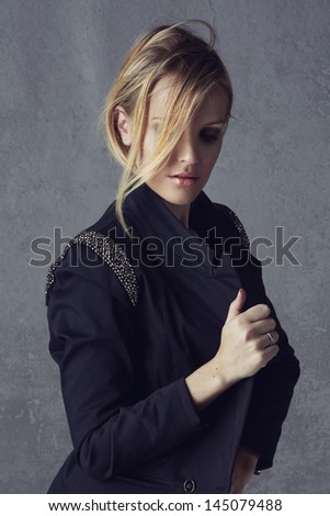 beautiful young blond woman with messy hair in a black blazer on grunge studio background