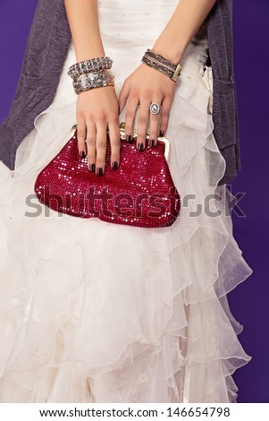 closeup of bride wearing ruffles dress and red luxury bag with fashion bangles and large diamond ring on purple studio background