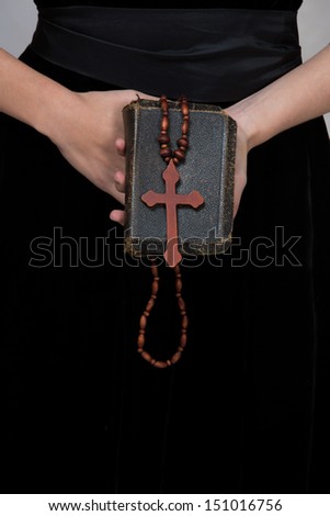 closeup of antique leather torn book with a christian cross in hands of a young woman held against black dress