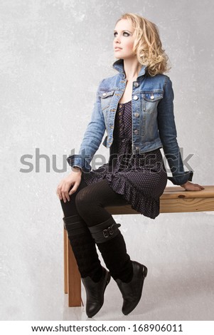 portrait of a young beautiful woman with loose curly hair blond hair wearing blue jean jacket with retro effect sitting on the bench