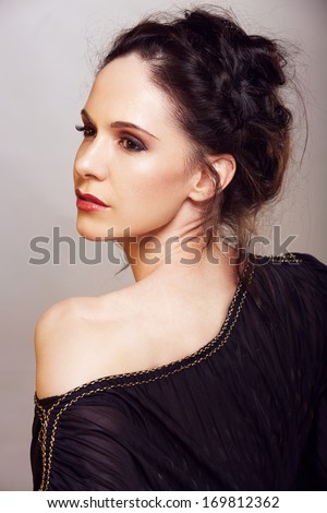 Beautiful woman with brown hair braided in upstyle wearing black off shoulder dress on studio background