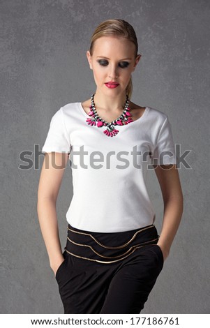 upper body portrait of a young blond woman wearing white t-shirt, statement pink necklace and black pants