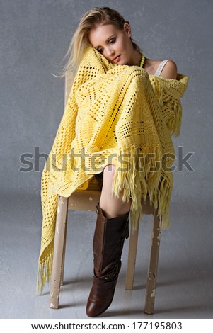 portrait of a beautiful woman with long blond hair sitting wrapped in crochet yellow blanket on grunge studio background