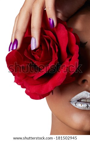 Closeup of woman\'????s face with silver lipstick. Tanned hand with purple metallic and texture manicure holding red fabric rose